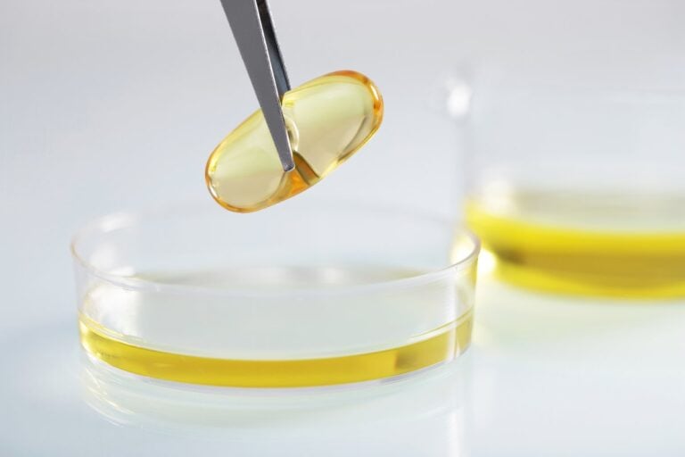 Unas pinzas sostienen una cápsula amarilla sobre un cuenco con aceite en un laboratorio