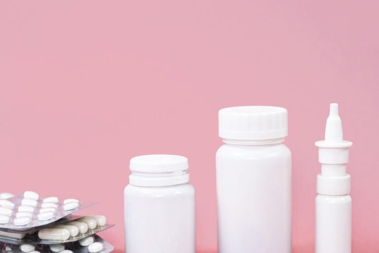 Frascos blancos para pastillas, blísteres y cápsulas esparcidas sobre un fondo rosa